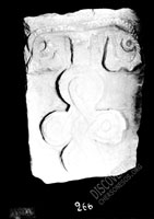 Stone with image of twisted cross on base shaped like scrolls or roots